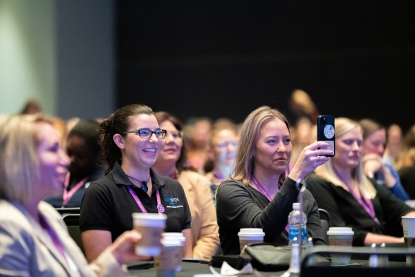 U.S. WIN members listen and laugh during a keynote address at the 2024 U.S. WIN national conference. The photo zooms in on two members actively listening to the speaker.